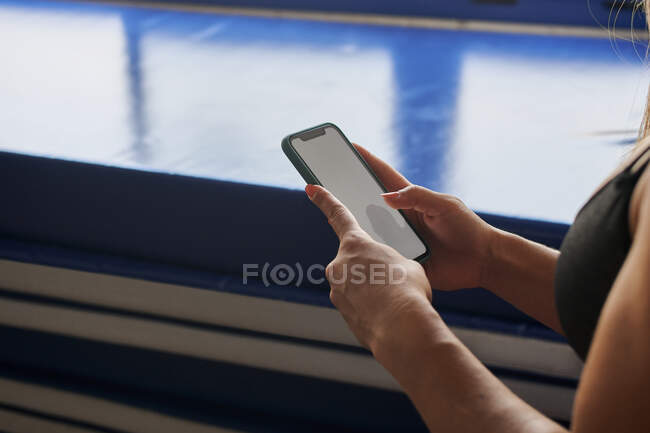 Side view of crop unrecognizable female athlete in bra surfing Internet on mobile phone with empty screen in gym — Stock Photo