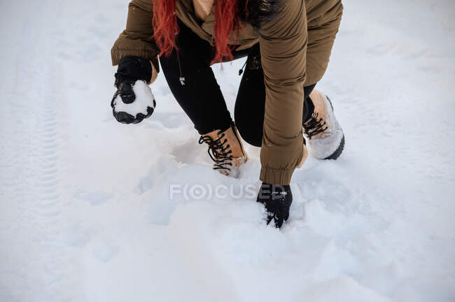 From above of crop unrecognizable female in outerwear taking snow for playing snowballs in winter — Stock Photo