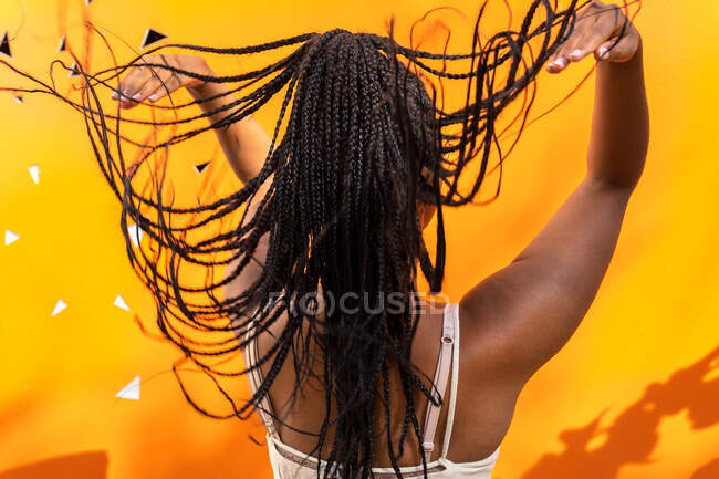 Rückansicht einer nicht wiedererkennbaren Afroamerikanerin, die in Barcelona lange geflochtene Haare auf leuchtend gelben Hintergrund wirft — Stockfoto