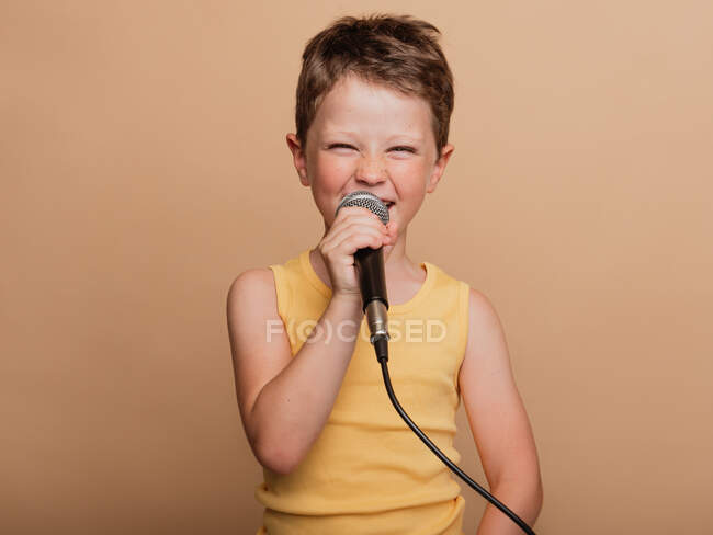 Cooles Kind beim Singen in modernem Mikrofon auf braunem Hintergrund im Studio — Stockfoto