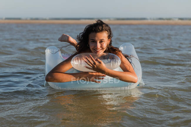 Вміст жінка лежить на надувному матраці, що плаває на морській воді в сонячний день влітку і дивиться на камеру — стокове фото