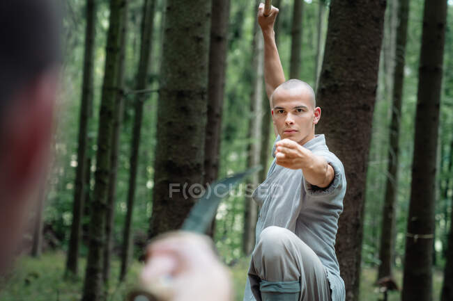 Мужчины в серой одежде практикуют кунг-фу с палкой и мечом во время тренировок в лесу — стоковое фото