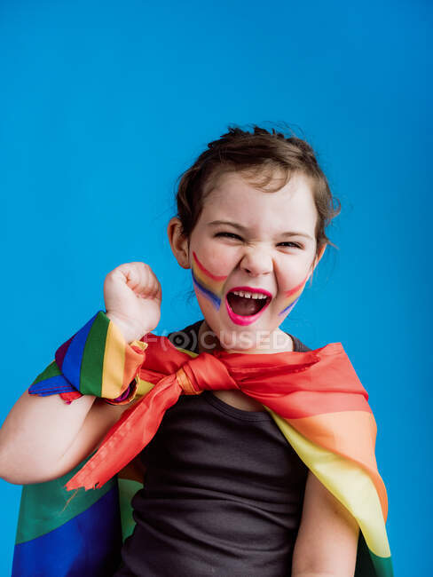 Мила щаслива дитина з різнокольоровою пов'язкою на шиї і зап'ястям, стоячи на синьому фоні і дивлячись на камеру — стокове фото
