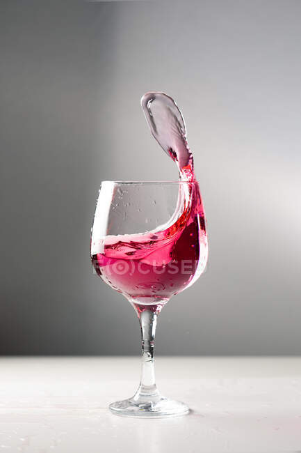 Alcol freddo bevanda rossa spruzzi di calice di vetro su sfondo grigio in studio — Foto stock
