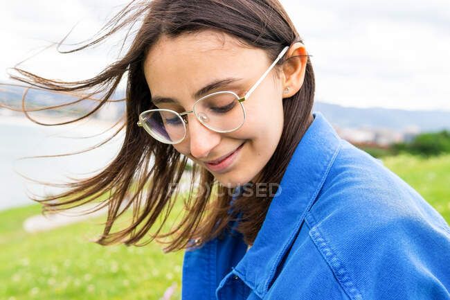 Mulher encantada com os olhos fechados sentados na colina verde e desfrutando de vista para o mar no dia nublado — Fotografia de Stock