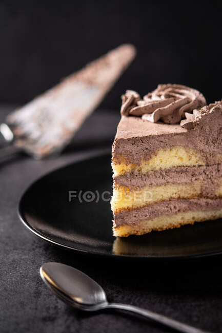Von oben ein Stück köstlicher Trüffelschokoladenkuchen, serviert in Teller auf schwarzem Tisch mit Löffel und Spachtel — Stockfoto