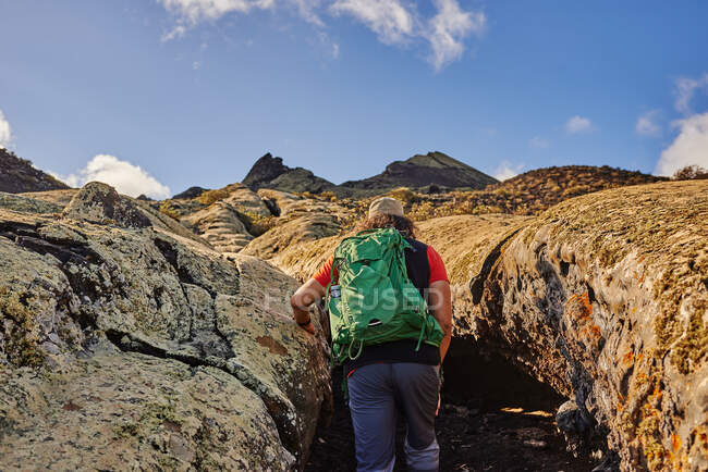 Анонімний турист з рюкзаком, який ходить по сухій стежці в долині біля пагорбів у похмурий літній день у Фуертевентурі (Іспанія). — стокове фото