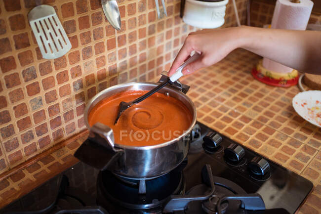 Високий кут врожаю безликі жінки готують перемішуючи гарячий соус маринари, приготований з помідорів у каструлі на плиті — стокове фото