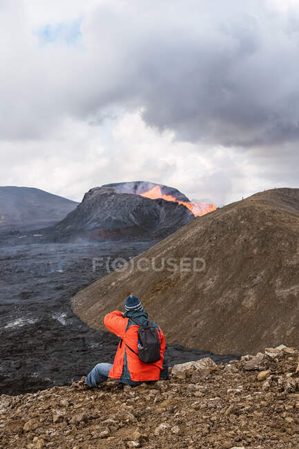 Vista posteriore del viaggiatore irriconoscibile seduto sul monte e contemplando Fagradalsfjall con fuoco in Islanda — Foto stock