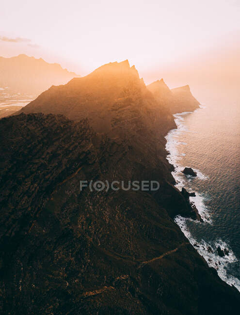 Magnífica paisagem aérea de terras altas rochosas perto do mar no fundo do céu brilhante do pôr do sol — Fotografia de Stock