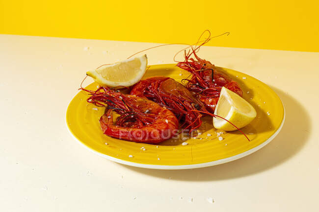 Fruits de mer savoureux de crevettes rouges cuites avec des tranches de citron frais et du sel grossier sur fond de deux couleurs — Photo de stock
