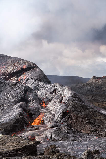 Vista panorâmica de Fagradalsfjall com fogo e lava contra montes sob céu nublado no dia ensolarado na Islândia — Fotografia de Stock
