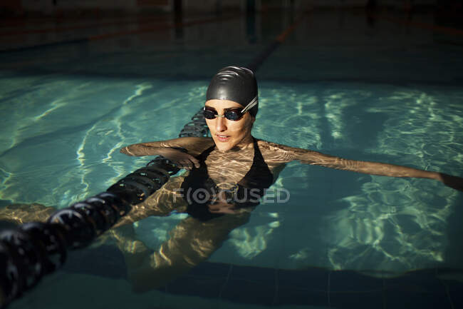 Jovem mulher bonita dentro da piscina interior, vestindo um maiô preto e segurando a barcaça de natação — Fotografia de Stock