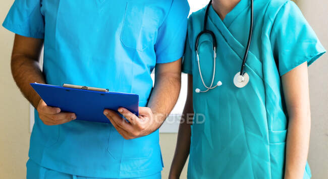 Anonymous male and female medics reading report on clipboard while standing in corridor in clinic — Stock Photo