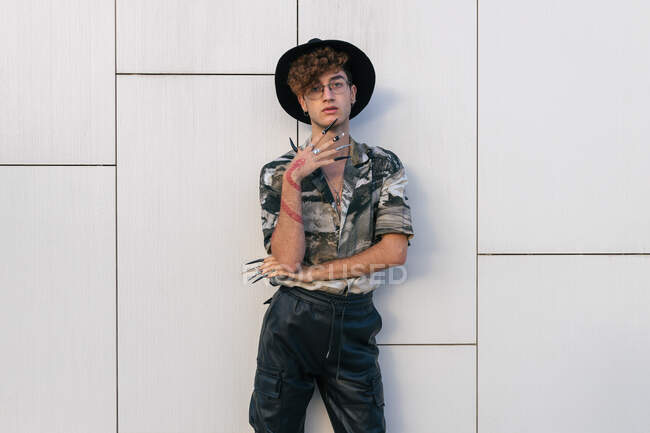 Giovane uomo vanitoso in elegante usura con cappello in piedi sulla parete piastrellata guardando la fotocamera — Foto stock