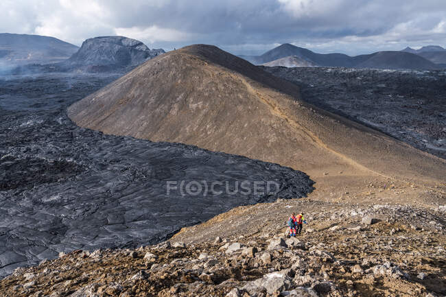 Randonneurs se promenant sur la montagne contre Fagradalsfjall avec lave et fumée sous un ciel nuageux en Islande — Photo de stock
