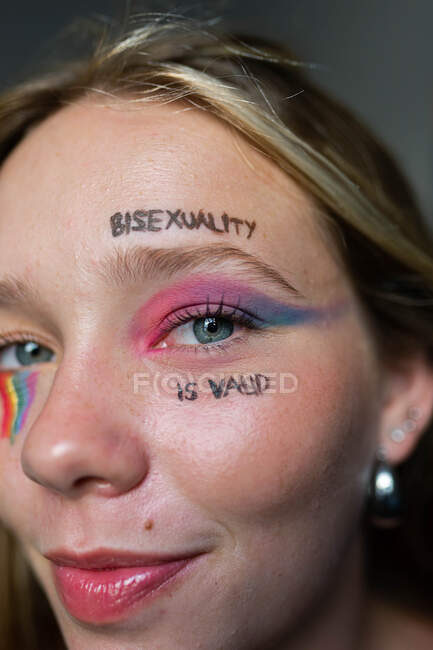 Mulher lésbica com inscrição no rosto Bissexualidade é válida e arco-íris Bandeira LGBT olhando para a câmera — Fotografia de Stock