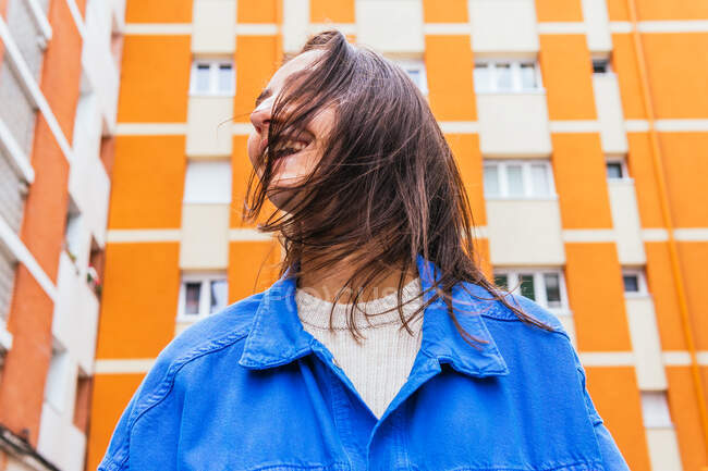 Низький кут весела жінка стоїть на вулиці проти яскравої будівлі і сміється — стокове фото