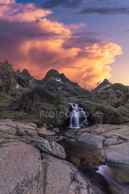 Vista panorámica de la Sierra de Gredos con cascada y estanque con fluidos de agua espumosa bajo el cielo nublado al atardecer - foto de stock