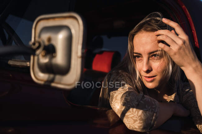 Stylish female driver looking in rear view mirror of vintage car on sunny day — Stock Photo