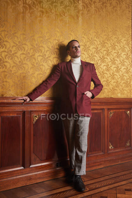 Selbstbewusster erwachsener männlicher Schauspieler in eleganter, stilvoller Kleidung, der die Hand in der Tasche hält und nachdenklich wegschaut, während er an der Wand im Vintage-Zimmer steht — Stockfoto
