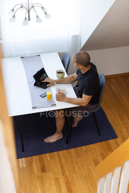 From above of male surfing Internet on tablet while sitting at table at home and enjoying breakfast in morning — Stock Photo