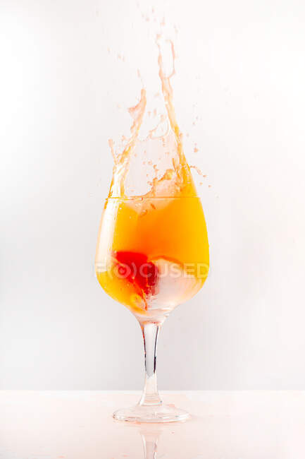 Cocktail arancio rinfrescante spruzzando in calice di vetro lucido su sfondo grigio in studio — Foto stock
