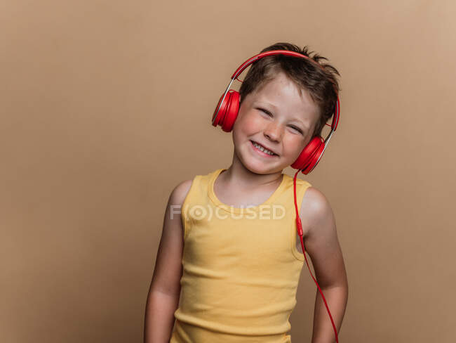 Niño preadolescente satisfecho en auriculares rojos escuchando música sobre fondo marrón en el estudio - foto de stock