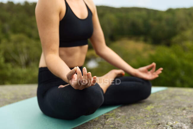 Anonyme junge Frauen schließen die Augen, während sie im Lotus meditieren, posieren auf einem Stein in der Landschaft — Stockfoto