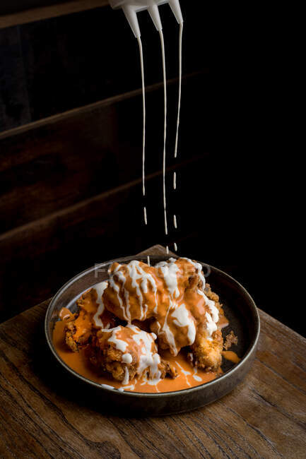 Dall'alto di salsa saporita che versa su pollo croccante messo su piatto rotondo su tavolo di legno in ristorante — Foto stock