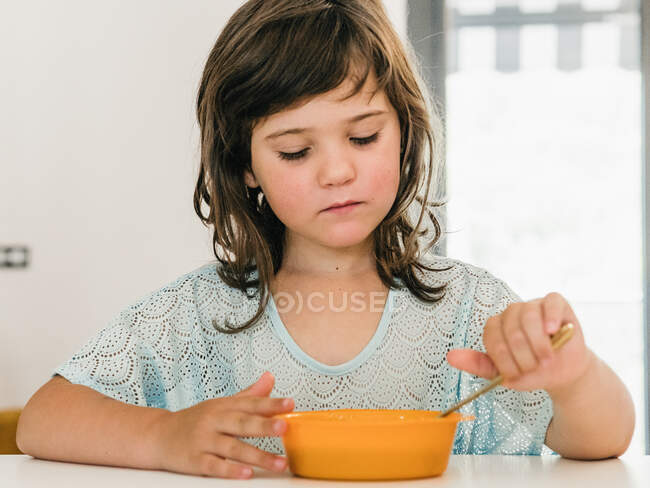 Девушка смотрит вниз на пластиковую миску, сидя за столом во время обеда дома — стоковое фото