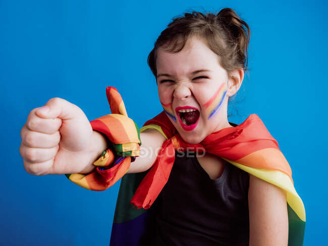 Criança feliz bonito com bandagem multicolorida no pescoço e pulso em pé contra o fundo azul e olhando para a câmera — Fotografia de Stock