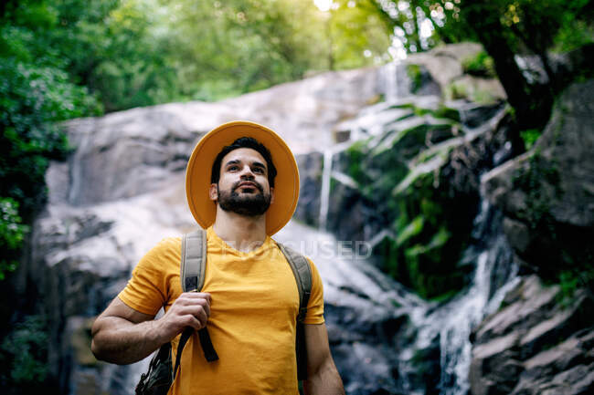 Von unten stehen männliche Wanderer auf Felsbrocken und neben Wasserfall und schauen im Wald weg — Stockfoto