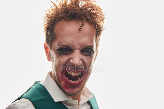 Excéntrico actor masculino con maquillaje manchado gritando de rabia mientras realiza sobre fondo blanco - foto de stock