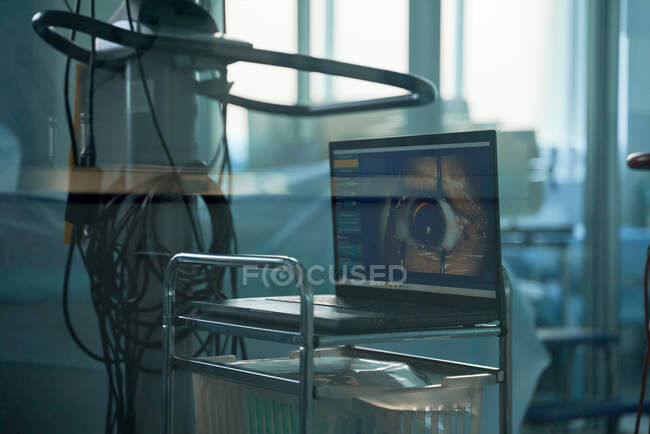 Through glass wall view of netbook with photography of human eye on screen in operating room — Stock Photo