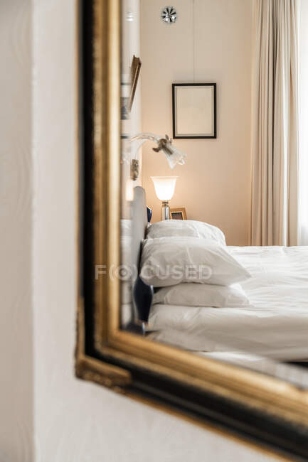 Interior do quarto moderno com cama macia com almofadas refletindo no espelho pendurado na parede — Fotografia de Stock