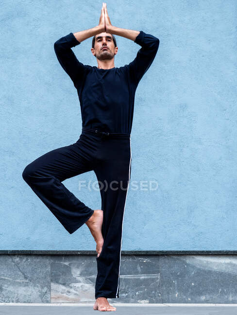 Low angle of serene ethnic male standing in Vrikshasana on street and practicing yoga — Stock Photo