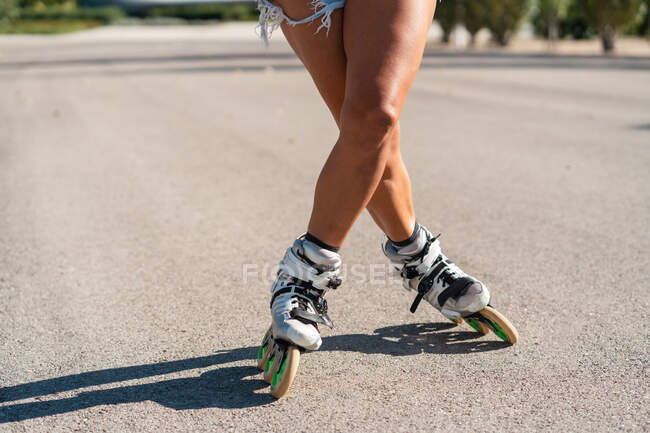 Обрезанная неузнаваемая женщина в роликах показывает трюк на дороге в городе летом — стоковое фото