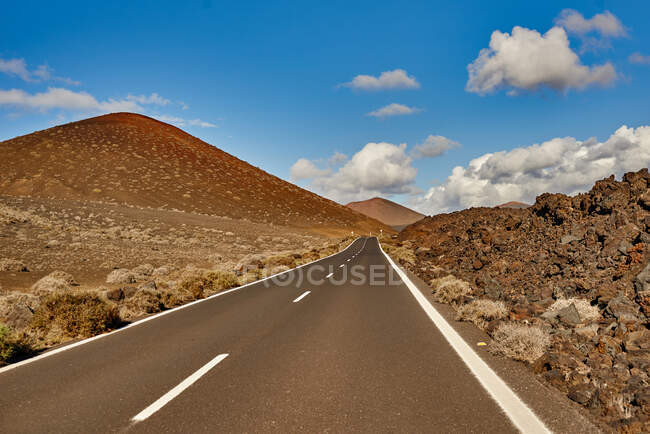 Estrada de asfalto em linha reta que atravessa o campo em direção ao passeio de montanha pela manhã em Fuerteventura, Espanha — Fotografia de Stock