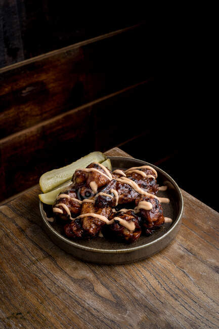 De cima de deliciosas asas de frango grelhado em molho de churrasco servido com pepinos no prato em mesa de madeira no restaurante — Fotografia de Stock