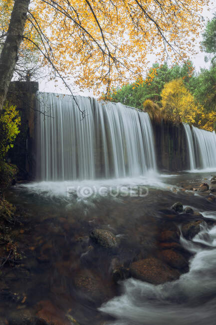 Сценічний вид на гору з каскадами і річкою з піноплавною водою на каменях між осінніми деревами в Лозої (Мадрид, Іспанія).. — стокове фото