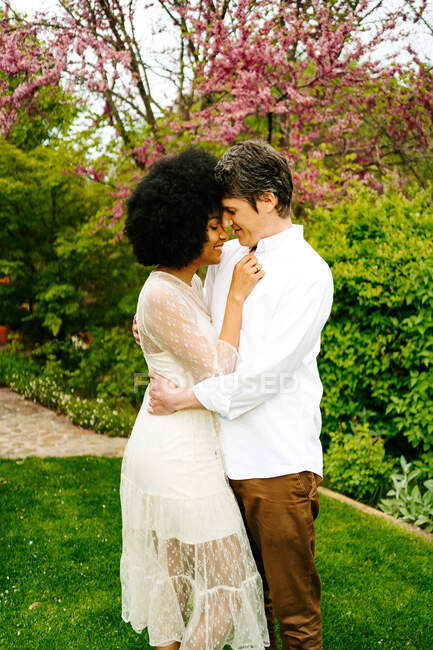Side view of man embracing black woman while standing on meadow in garden — Stock Photo