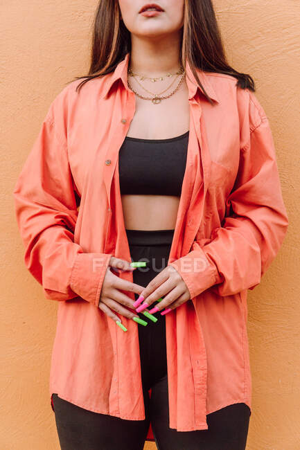 Cultiver femelle méconnaissable avec de longs ongles colorés portant chemise lumineuse debout près du mur orange — Photo de stock