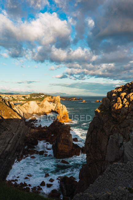 Spectaculaire paysage de rivage rocheux rugueux baigné par des vagues de mer mousseuses au soleil sous un ciel nuageux bleu à Liencres en Cantabrie en Espagne — Photo de stock