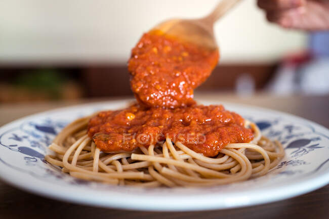 Closeup of unrecognizable cook garnishing tasty spaghetti with marinara sauce prepared for lunch — Stock Photo