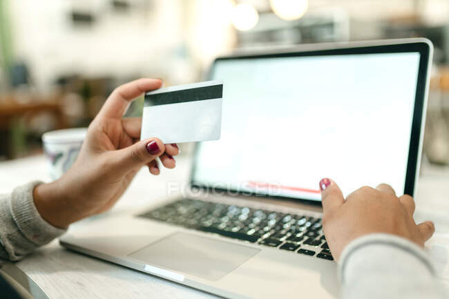 Crop unrecognizable female making purchase with plastic card for order during online shopping via laptop — Stock Photo