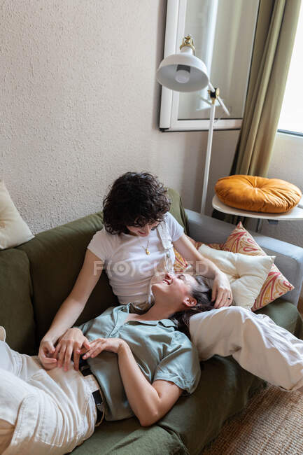 Tender lesbian woman lying on knees of loving girlfriend sitting on couch at home and relaxing during weekend — Stock Photo