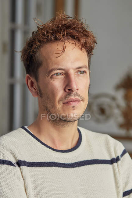 Schöner rothaariger Mann mit welligem Haar, der vor verschwommenem Hintergrund nachdenklich wegschaut — Stockfoto