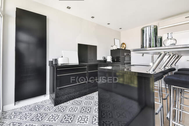 Moderno diseño interior de la casa de amplia cocina abierta con muebles negros y azulejos ornamentales en el piso y con grandes ventanas panorámicas con vistas a edificios urbanos - foto de stock