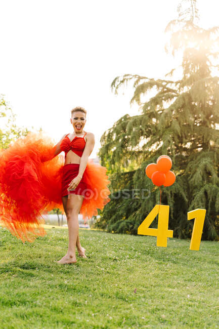 Trendy black female with decorative numbers and red balloons standing barefoot in park during birthday party in sunlight — Stock Photo